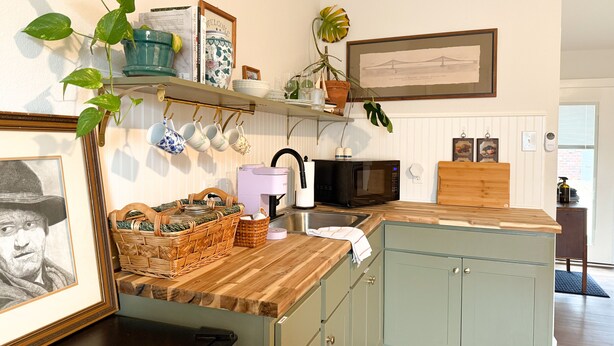 Une cuisine dotée de plans de travail en bois, d’un évier, d’un four à micro-ondes et d’une machine à café. On y trouve également des étagères ornées d’objets décoratifs et de plantes.