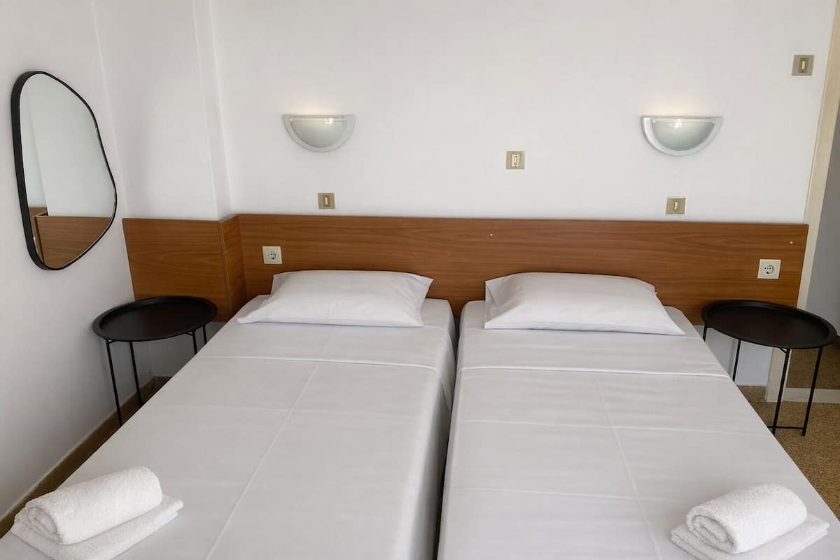 Een hotelkamer met twee eenpersoonsbedden, een houten hoofdbord, nachtkastjes, een wandspiegel en wandlampen.