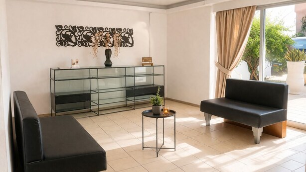 Ein modernes Wohnzimmer mit einem Glastische, zwei schwarzen Sofas, einem kleinen runden Tisch mit Pflanze und einem dekorativen Wandbild.