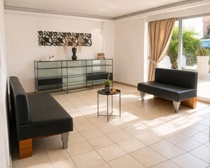 Een moderne woonkamer met een glazen console tafel, twee zwarte banken, een kleine ronde tafel met een plant en een decoratief kunstwerk aan de muur.