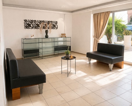 A modern living room with a glass console table, two black sofas, a small round table with a plant, and a decorative wall piece.