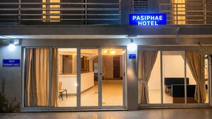 Ein Hotel Eingang mit einem Schild, auf dem 'PASIPHAE HOTEL' steht, Glastüren und einem einsehbaren Innenbereich mit Sitzmöglichkeiten.