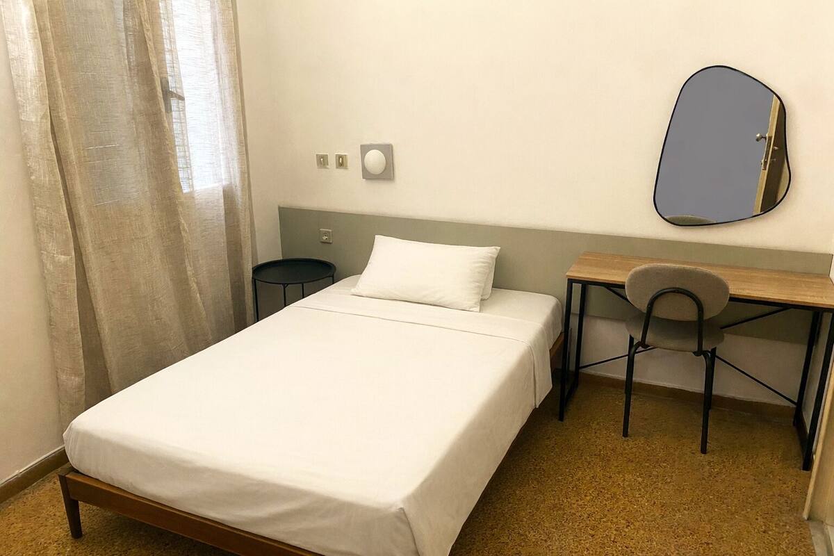 Een hotelkamer met een bed, een bureau, een stoel, een ronde tafel en een spiegel.