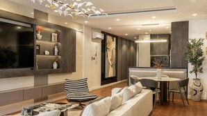 A modern living room with a large L-shaped sectional sofa, a dining area with a round table, and a TV mounted on the wall. - Luxury apartment with pool, gym & games (Lekki)