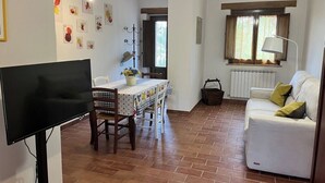 Ein Wohnzimmer mit weißem Sofa, einem Esstisch mit Stühlen, einem Fernseher, einem Deckenventilator und Kunstwerken an den Wänden.