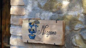 Eine Steinmauer mit einem Holzschild, das "Niagara" zeigt und eine blaue Armatur sowie eine Illustration eines Topfpflanzes enthält.