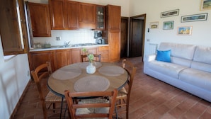 A kitchen with wooden cabinets, a dining table with placemats, a white sofa, and a tiled floor. - Farmhouse Il Mulino delle Canutole - Pienello (Magione)