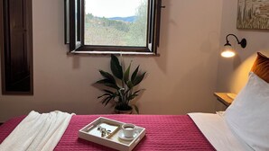 A room with a bed, a window with a view of greenery, a bedside table with a lamp, and a tray with a cup and a box. - Farmhouse Il Mulino delle Canutole - Pienello (Magione)