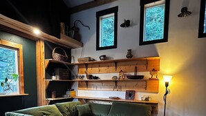 Ein gemütliches Wohnzimmer mit einer Eckcouch, Holzbalken, Regalen mit Dekoration und einem gemusterten Teppich.