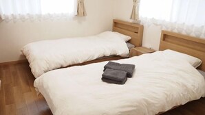 A double bed with a white bedspread and two pillows, a wooden nightstand, and a wooden headboard. - Western-style house for families and groups (Okuma)