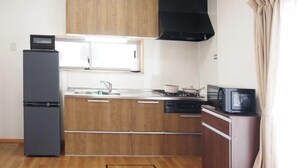 A kitchen with wooden cabinets, a refrigerator, a microwave, and a stove. - Western-style house for families and groups (Okuma)
