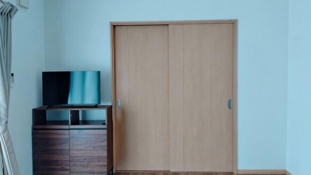 A room with a wooden wardrobe, a television on a wooden cabinet, and a light blue wall. - Western-style house for families and groups (Okuma)