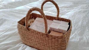 A wicker basket with handles containing several items on a white bedspread. - Western-style house for families and groups (Okuma)