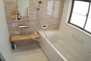 A modern bathroom with a bathtub, a shower, a vanity, and a window. - Western-style house for families and groups (Okuma)