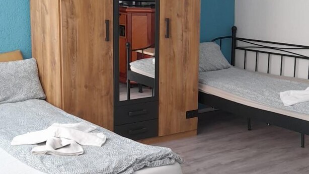 A bedroom with two beds, a wardrobe, and a small kitchenette. - Hotel Feiertag (Pforzheim)