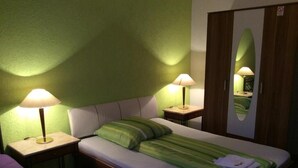 A single bed with a green striped blanket, two bedside lamps, a mirror, and a wooden wardrobe. - Hotel Feiertag (Pforzheim)