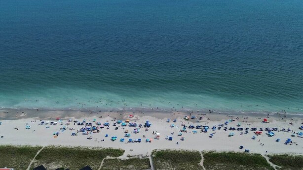 Une plage avec de nombreux parasols et beaucoup de monde, ce qui indique qu’il s’agit d’un lieu touristique très fréquenté.