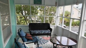 Une véranda avec un tapis à motifs, deux fauteuils en osier, une petite table et une vue sur l’extérieur.
