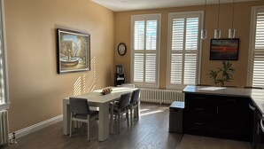 Uma sala de jantar com mesa, cadeiras, máquina de café e radiador.