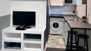 Cocina compacta con electrodomésticos integrados, lavadora y televisor sobre un mueble blanco.