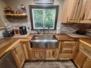 A kitchen with a stainless steel sink, wooden cabinets, a window with a view of greenery, and a coffee maker. - Charming 3-bedroom house overlooking Otsego Lake in Gaylord wih Sunset Views! (Gaylord)