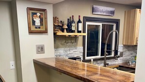 Eine moderne Küche mit Holztresen, zwei Barhockern, einem integrierten Weinkühlschrank und einem Edelstahlkühlschrank.