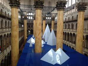 Un vaste hall aux colonnes de marbre et au sol bleu, agrémenté de grandes sculptures géométriques blanches.