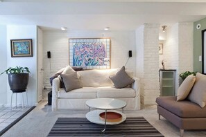 Un salon moderne avec un canapé blanc, une table basse ronde et un tableau abstrait aux couleurs vives accroché au mur.