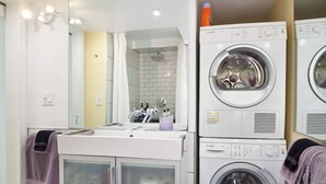 Een moderne badkamer met een wastafel, spiegel en gestapelde wasmachines.