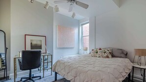 Een slaapkamer met een bed, een bureau, een stoel, een plafondventilator en een raam.