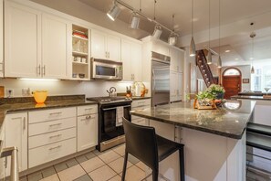 A modern kitchen with white cabinetry, stainless steel appliances, a marble countertop, and a built-in island with seating. - Downtown Victorian home w/Stunning Roof & Parking (Washington)