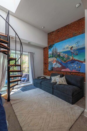 A modern living room with a staircase, a large mural, and a grey sofa. - Downtown Victorian home w/Stunning Roof & Parking (Washington)