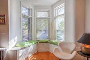 A corner room with a bay window, a radiator, a white chair, and a lamp on a table. - Downtown Victorian home w/Stunning Roof & Parking (Washington)