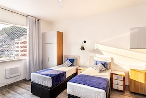 A modern hotel room with two beds, a large window with a view, a wardrobe, a desk, and a lamp. - Wish Copacabana - Praia (Rio de Janeiro)