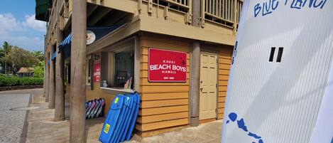 Ein restaurant im Strandhausstil mit einem Schild mit der Aufschrift "Kauai Beach Boys Hawaii" und einer blauen Surfbrett-Ausstellung draußen.