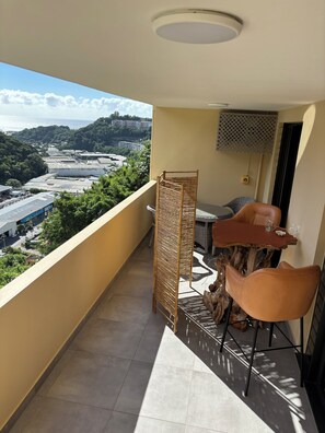 Un balcón con vistas a un paisaje urbano, una mesa con sillas y un adorno de madera.