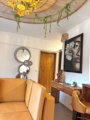 A room with a brown leather sofa, a wooden door, a desk with a vase, and a framed artwork on the wall.