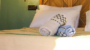 Una cama con dos toallas enrolladas, un aplique de pared y un cabecero de madera con un diseño geométrico.