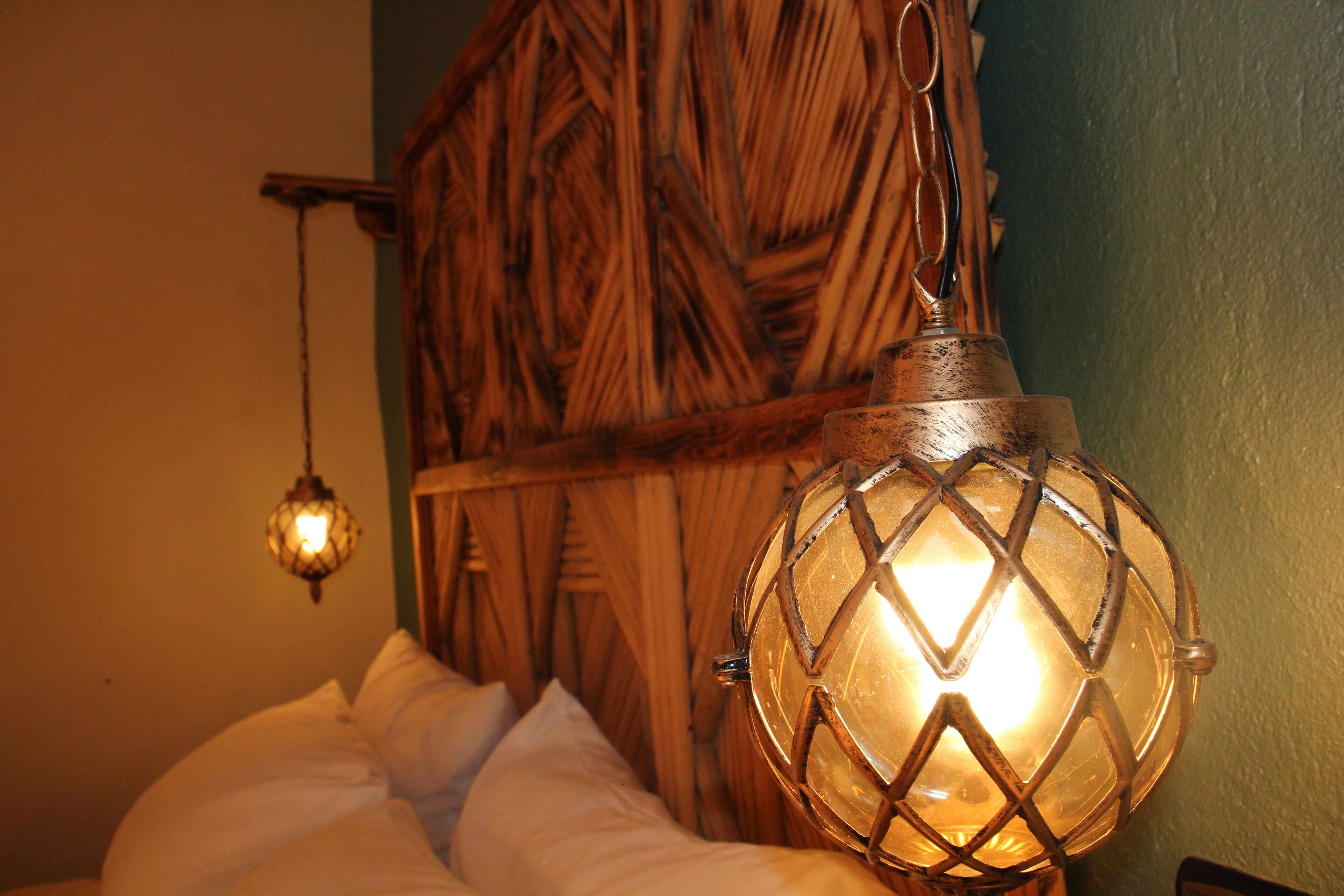 Un lit avec une literie blanche et un luminaire suspendu au design géométrique.