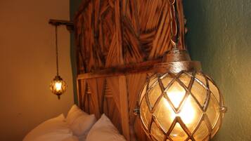 Un lit avec une literie blanche et un luminaire suspendu au design géométrique.