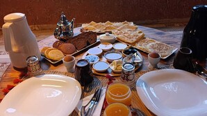 Una mesa de madera con desayuno servido, incluyendo platos, cubiertos y diferentes alimentos.