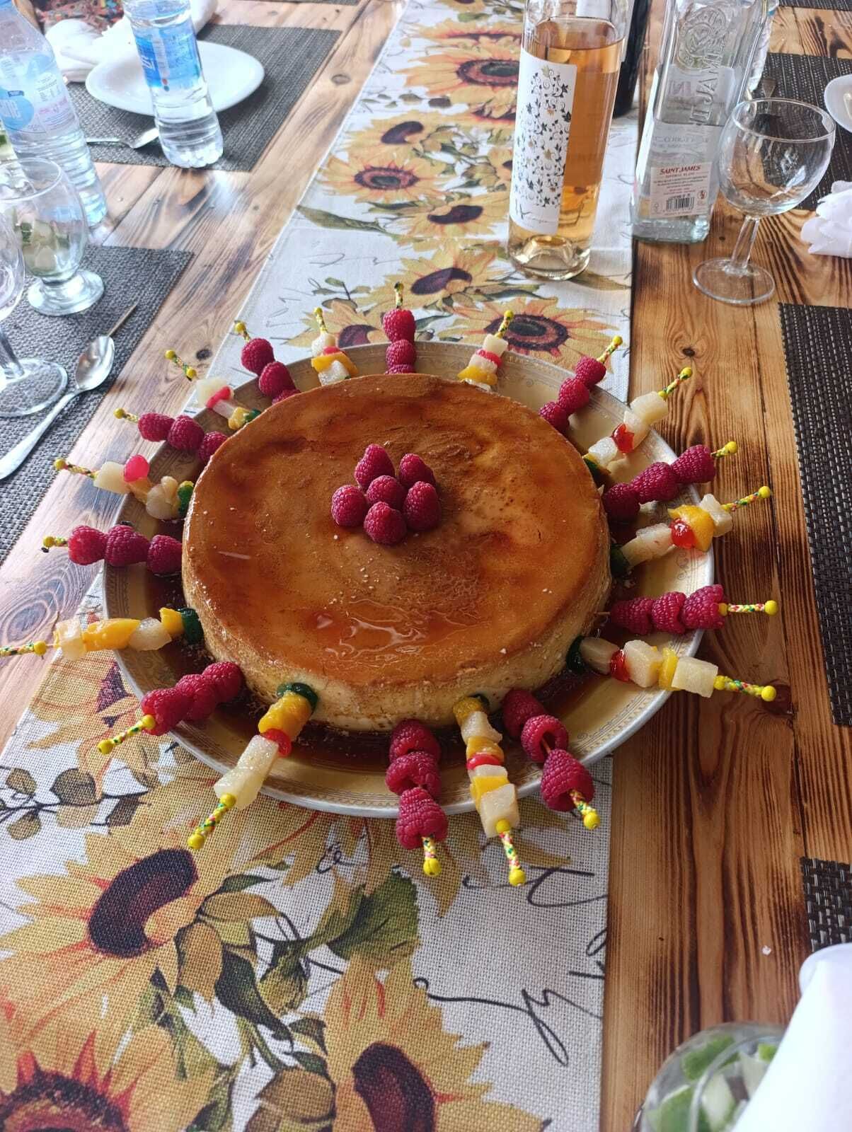 Un plato con postre, un pastel y brochetas de fruta sobre una mesa con mantel de flores.