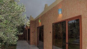 Fachada de un edificio con un camino, un árbol grande y una puerta con panel de vidrio.