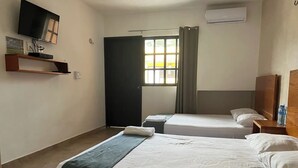 Habitación de hotel con dos camas, un televisor montado en la pared, una ventana con cortinas y un equipo de aire acondicionado.