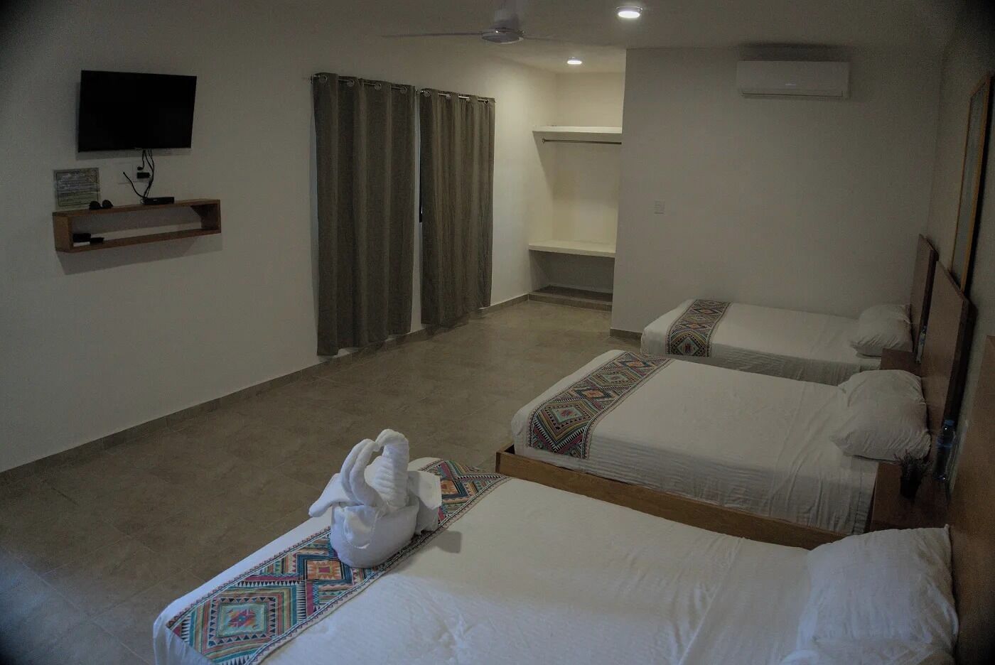 Habitación de hotel con dos camas, televisión, ducha y una pequeña estantería.