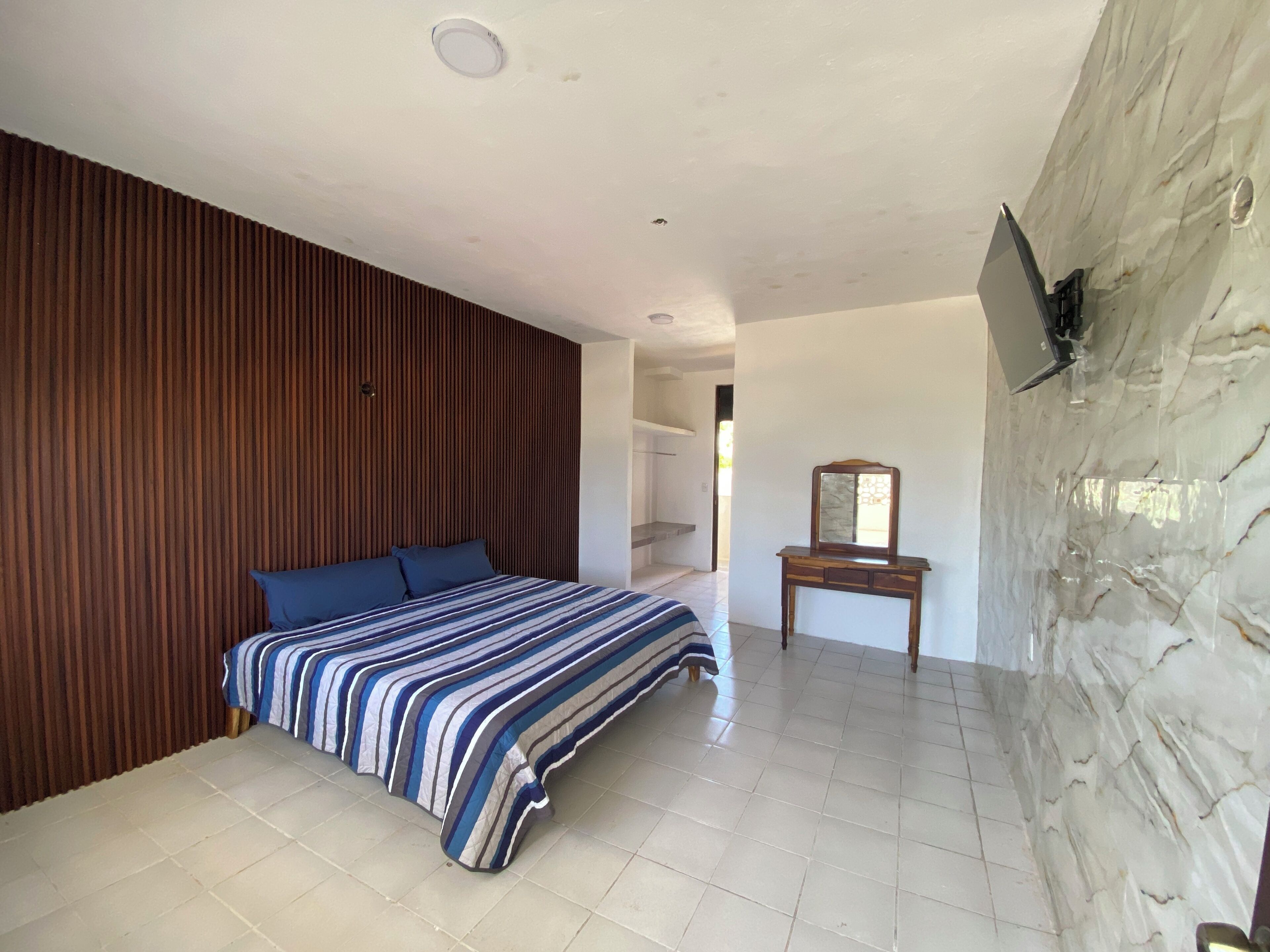 Un dormitorio con cama, cabecera de madera, mesita de noche con espejo y pared de piedra.