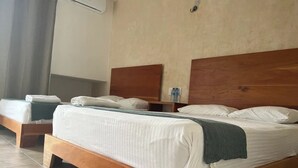 Una habitación de hotel con una cama grande, un cabecero de madera, una mesita de noche con una botella de agua y una cortina.