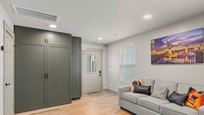 Een moderne woonkamer met een grijze bank, een stadslandschap schilderij en een grote kledingkast.