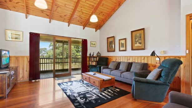 Uma sala de estar acolhedora com soalho de madeira, um sofá, uma mesa de centro e uma televisão. Há quadros nas paredes e uma estante de livros.