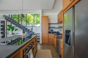 A modern kitchen with a central island, stainless steel appliances, wooden cabinets, and a staircase leading to a balcony. - Brand New Ocean & Mountain View Retreat in Guiones, Nosara (Guiones)